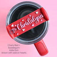 The top of a stanley tumbler shown with a solid red acrylic with the name Christalynn written in cursive in bubblegum pink acrylic font with the name surrounded by mini heart shapes.