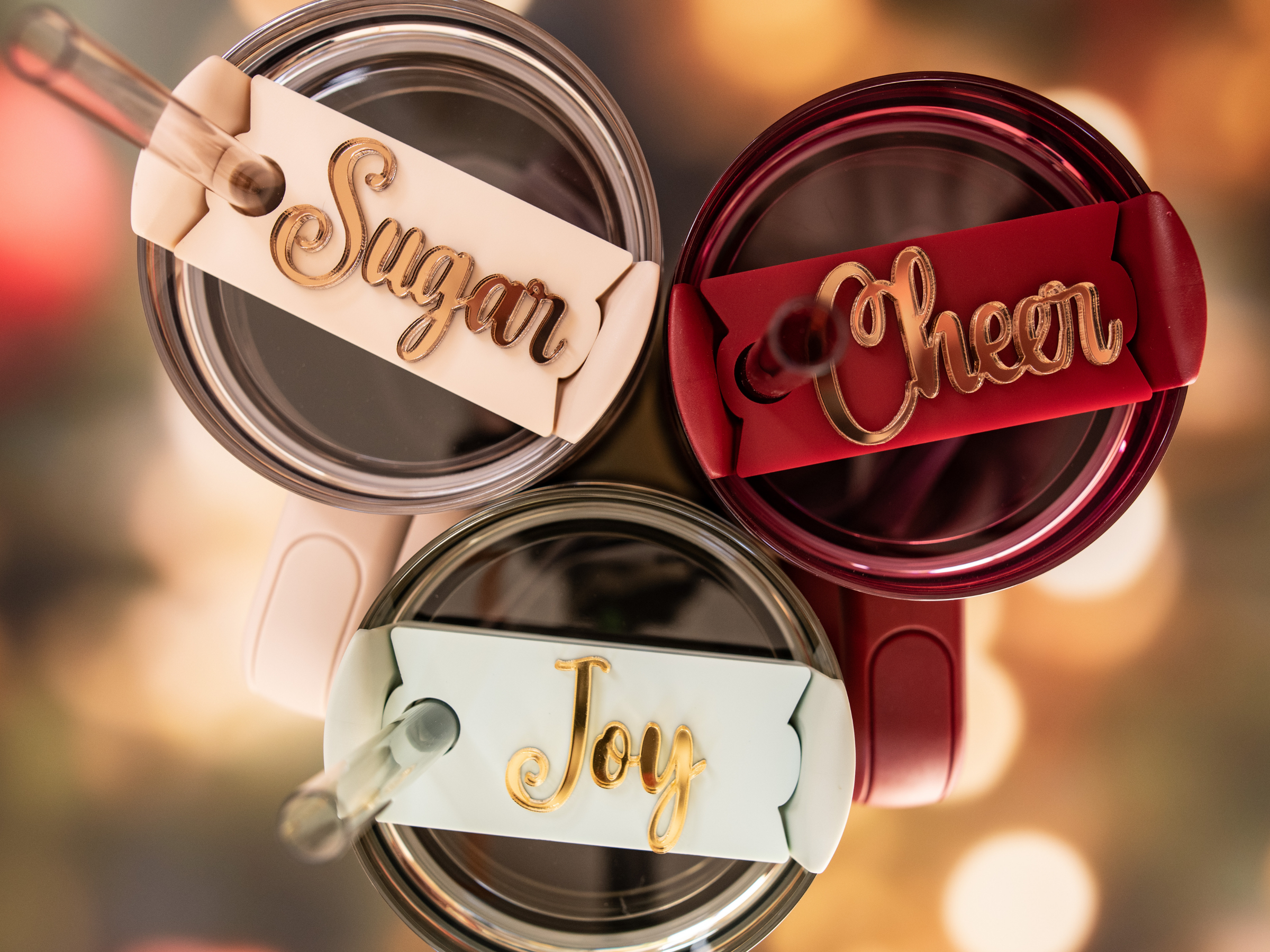 Three acrylic drink tumblers with personalized tags. Each tag has a different color— beige, red, and blue—with a golden script writing.