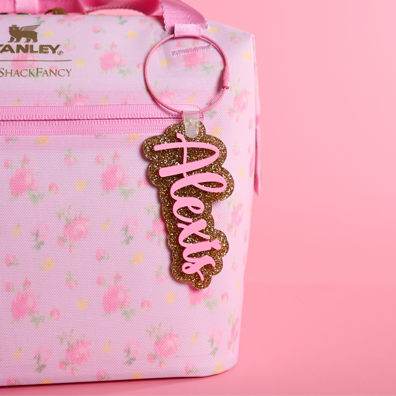 Love Shack Fancy Ibiza Sunset floral-patterned bag with a gold glitter and bubblegum bag tag
