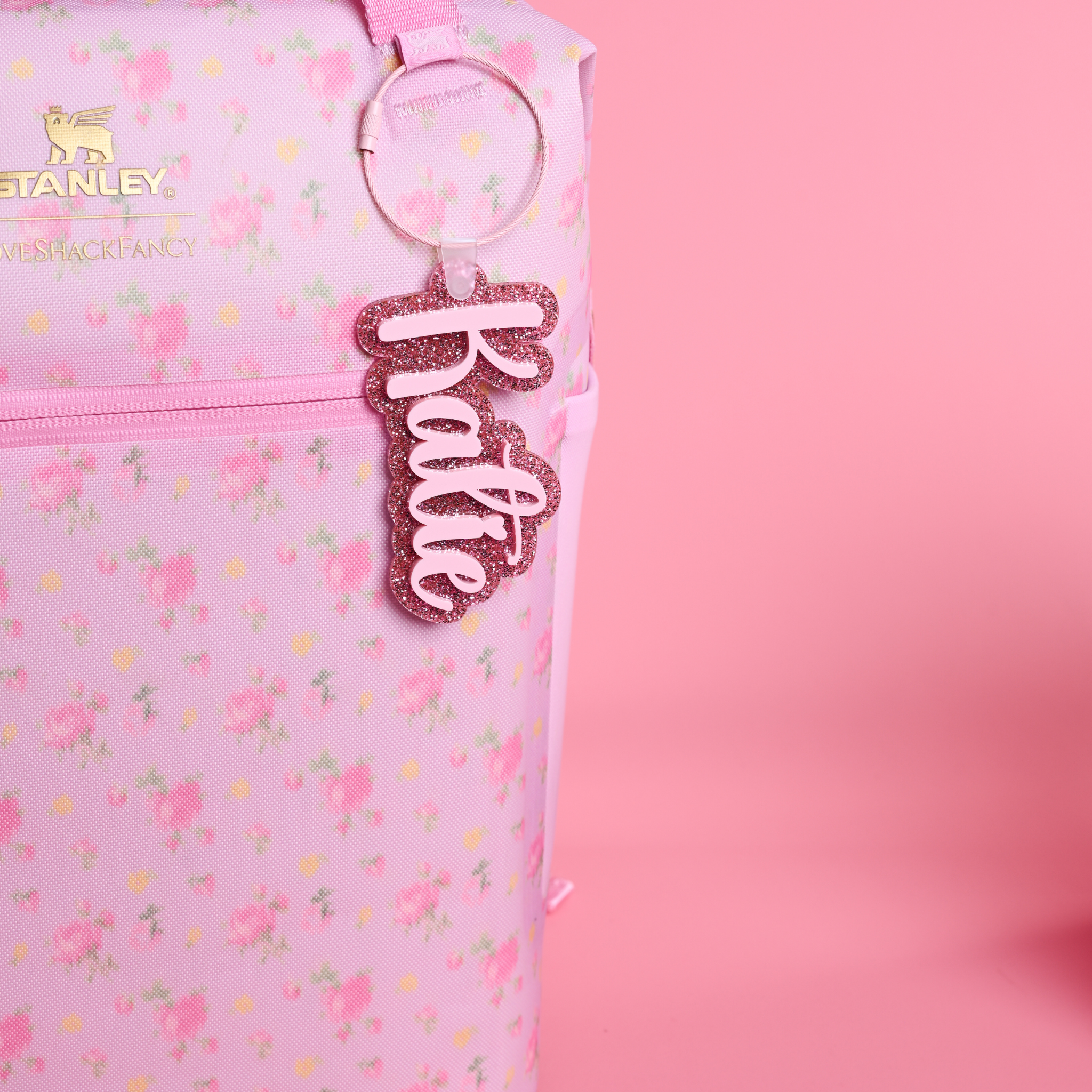 Love Shack Fancy Ibiza Sunset floral-patterned bag with a pink glitter and ballet pink bag tag