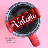 The top of a stanley tumbler shown with red chunky hex glitter acrylic with the name Valerie written in cursive in bubblegum pink acrylic font.
