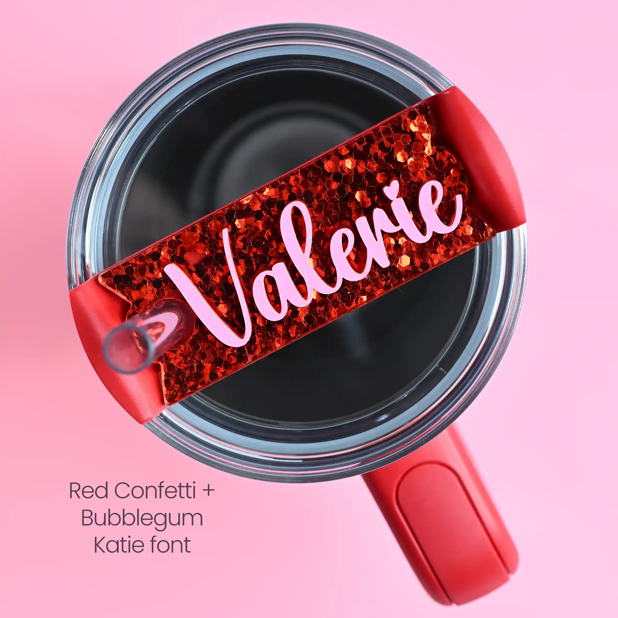 The top of a stanley tumbler shown with red chunky hex glitter acrylic with the name Valerie written in cursive in bubblegum pink acrylic font.