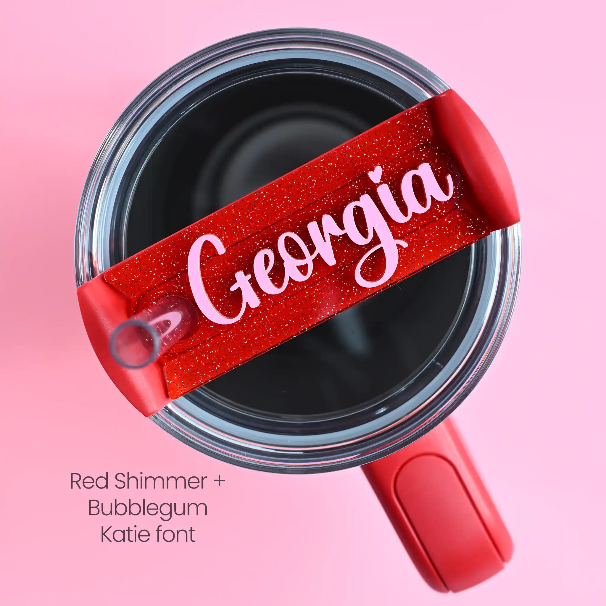 The top of a stanley tumbler shown with red shimmer acrylic with the name Georgia written in cursive in bubblegum pink acrylic font.