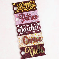 A collection of acrylic Topper Tag name plates designed for Stanley Quencher tumblers in burgundy, pink, and gold color tones.
