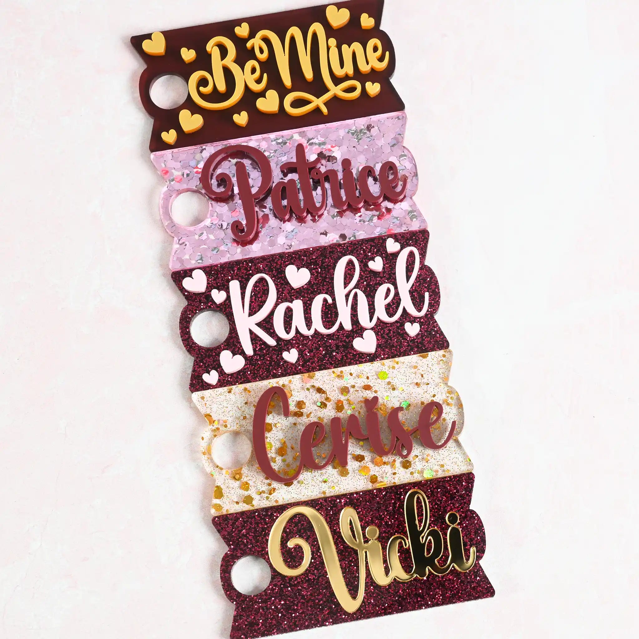 A collection of acrylic Topper Tag name plates designed for Stanley Quencher tumblers in burgundy, pink, and gold color tones.